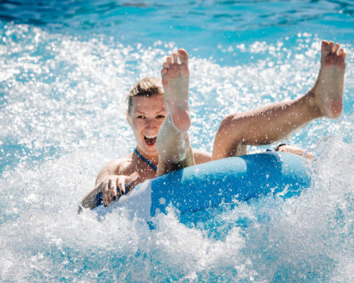 Happy girl taking a fast water ride on a float splashing water. Summer vacation with water park concept.